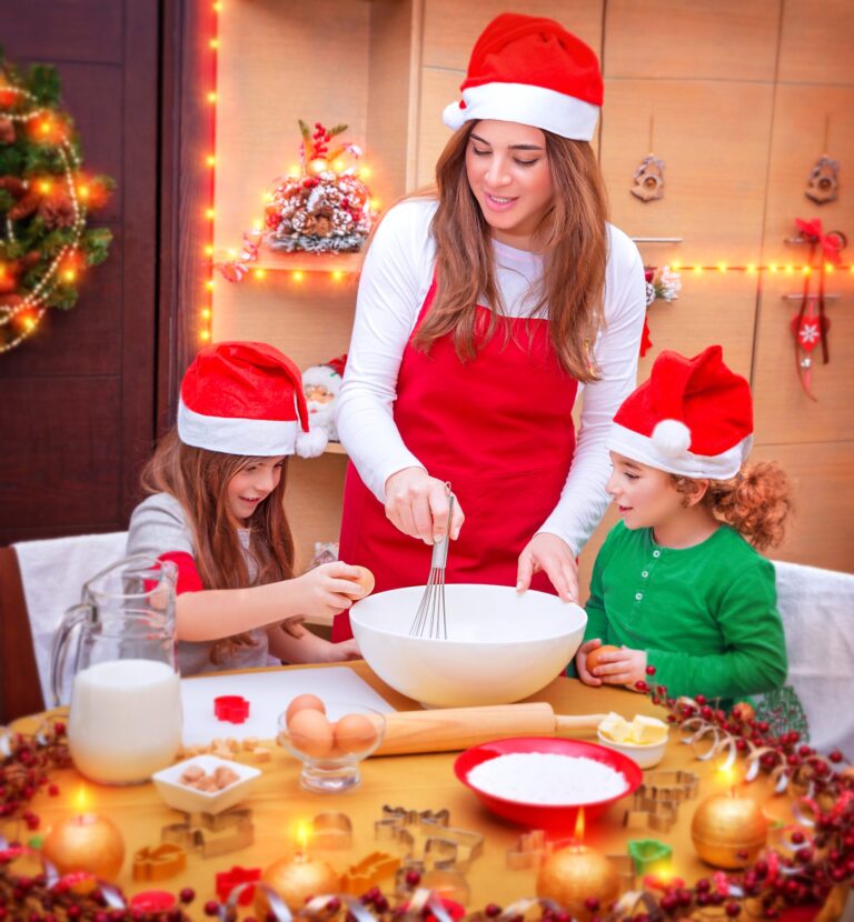 A mom and two children dressed in Christmas hats baking with eggs, milk, and butter